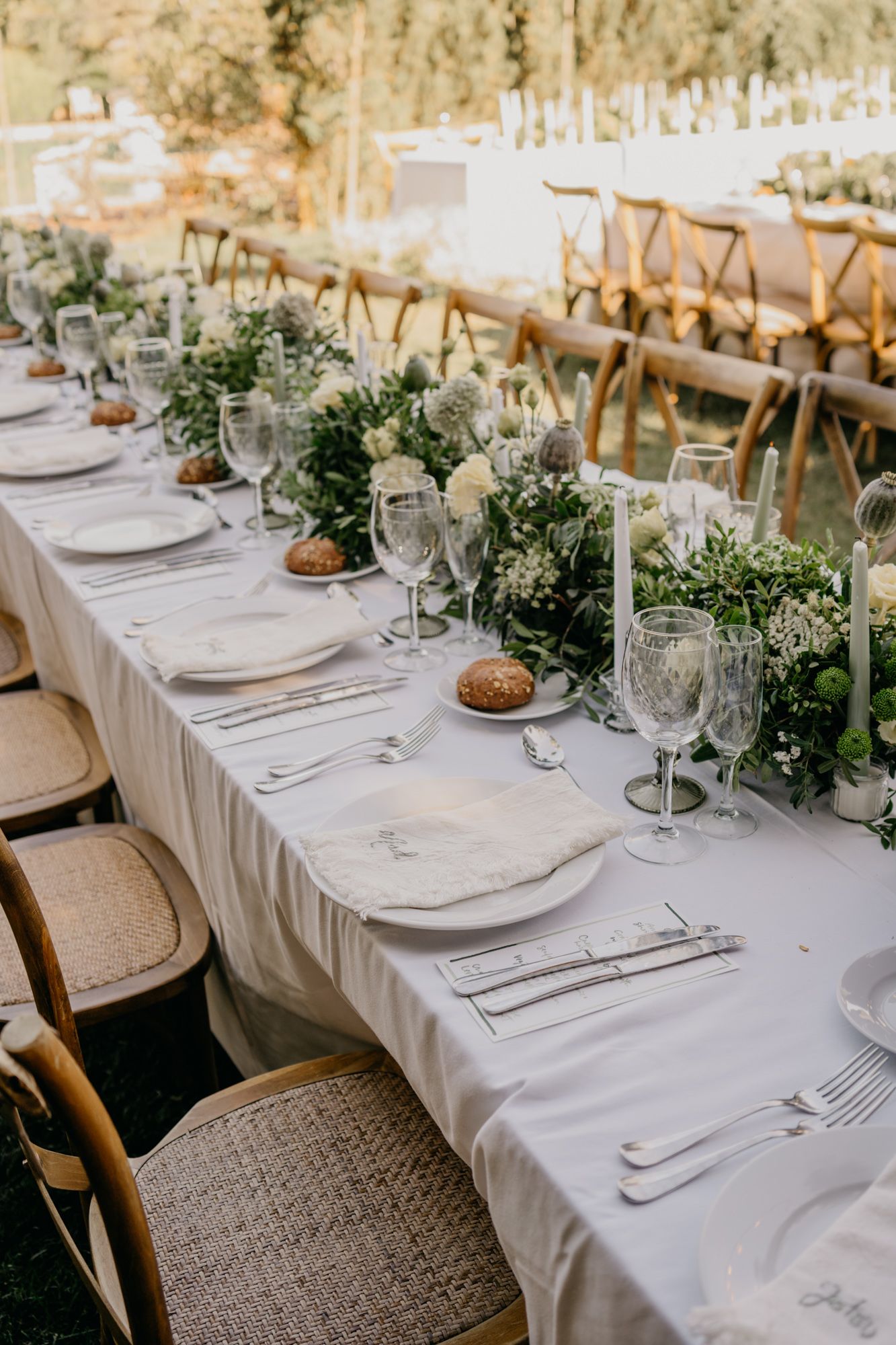Long dining table with white linens, crystal glasses, and natural green centerpieces.