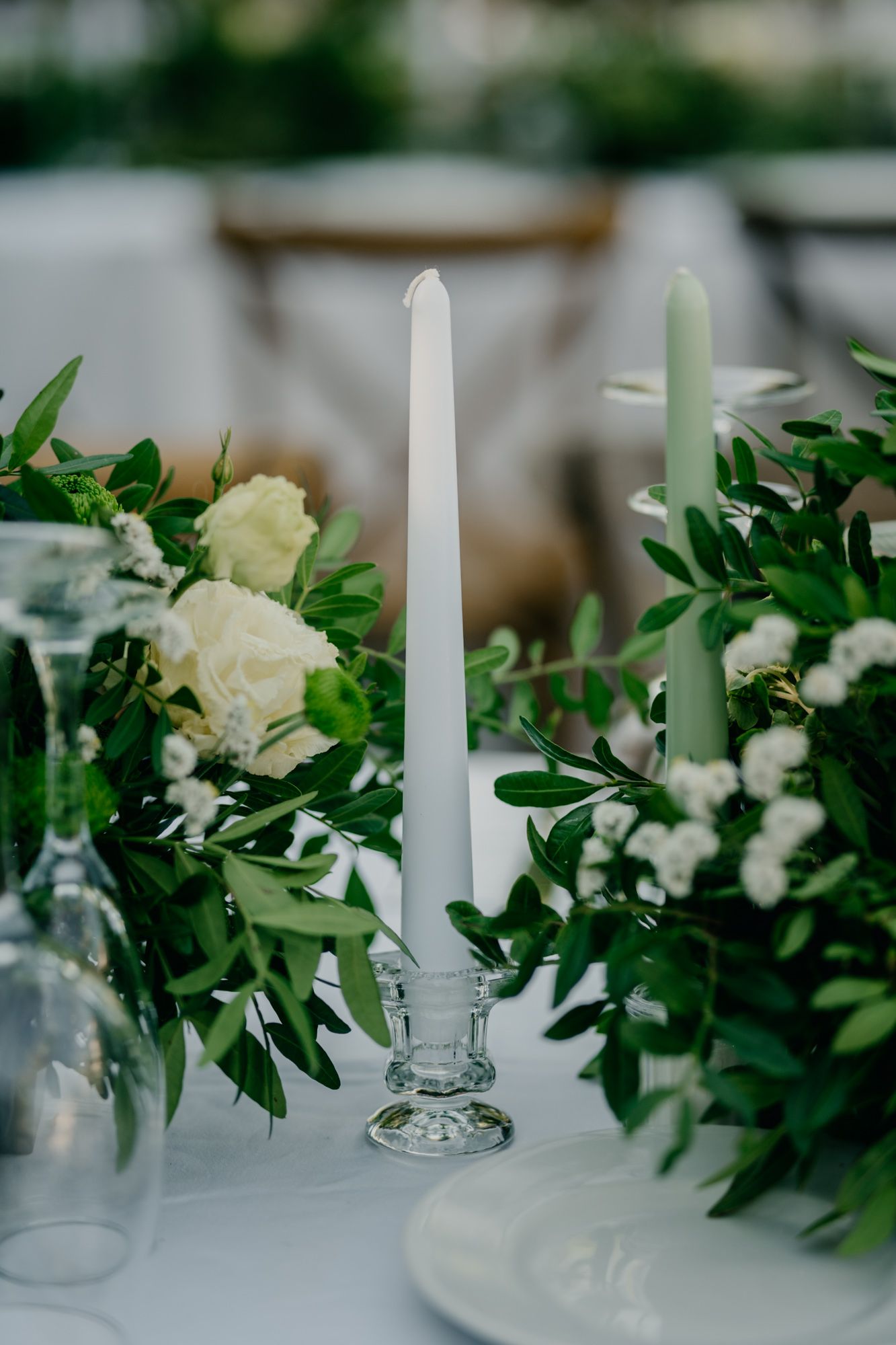 Elegant white and sage green taper candles surrounded by fresh floral arrangements.