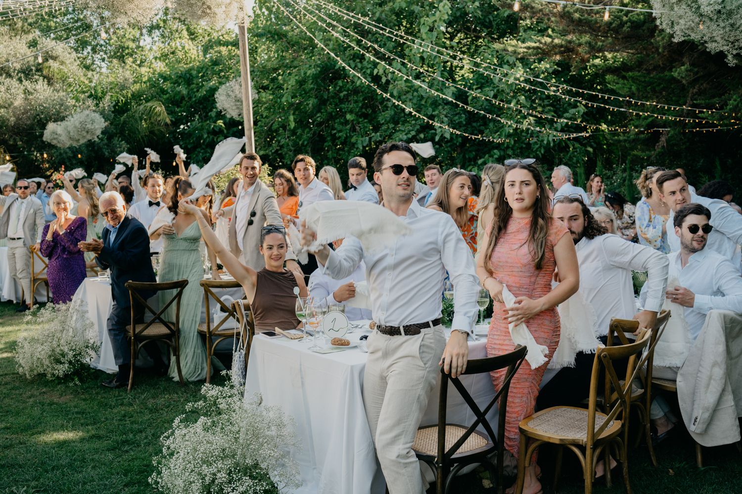 Outdoor wedding celebration with guests seated at decorated tables under string lights.
