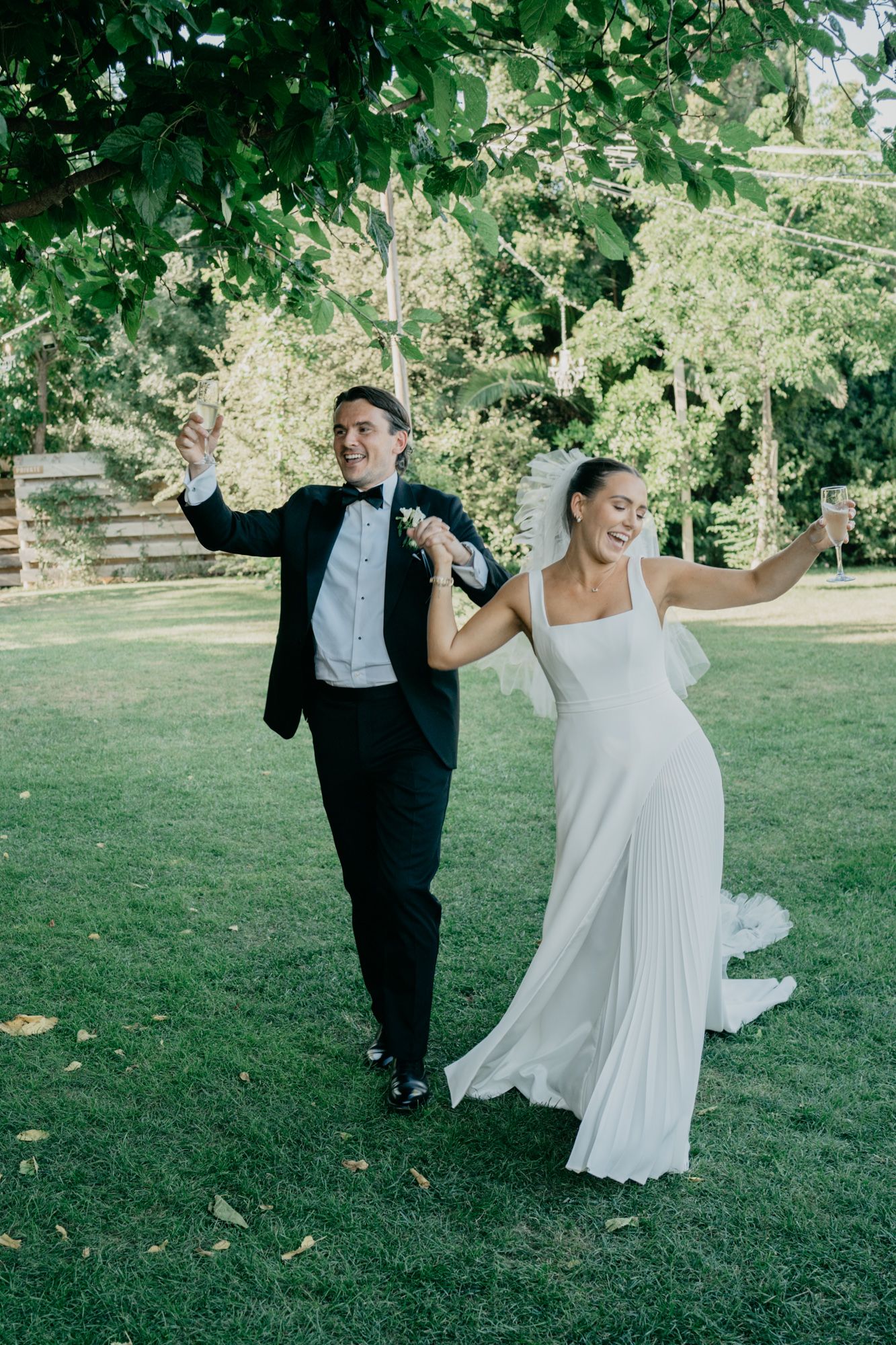 Wedding celebration on a green lawn with elegant attire and joyful movement.