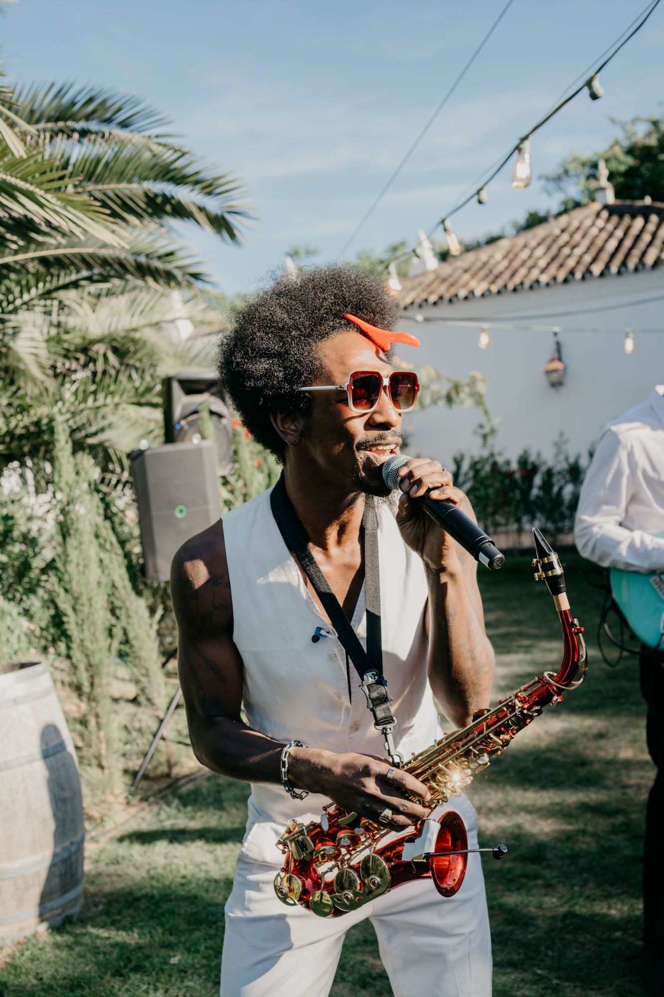 Musician performing with saxophone at outdoor event with string lights and palm trees.