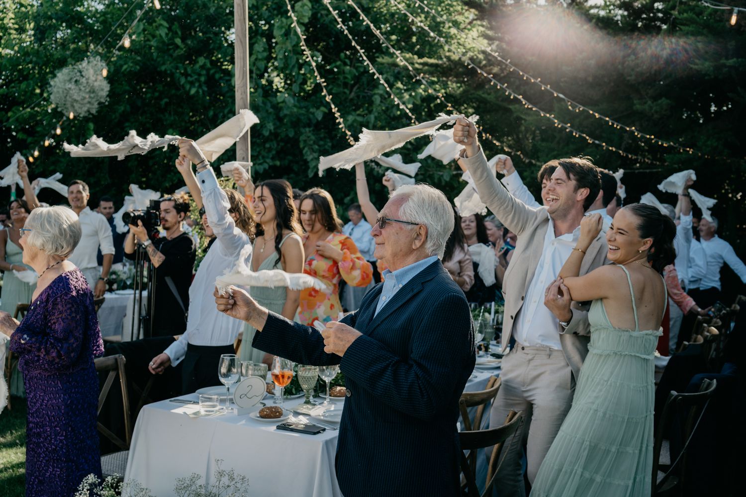 Wedding guests celebrating with napkins raised in the air during an outdoor reception celebration.