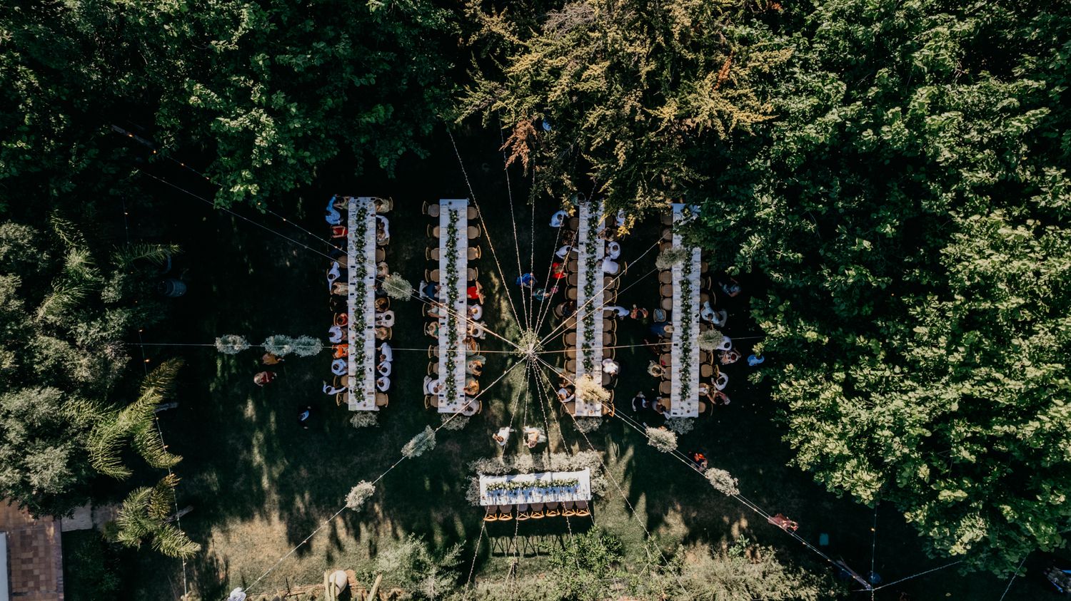 Overhead view of wedding seating arrangement with hanging lights and decorations in a garden setting.