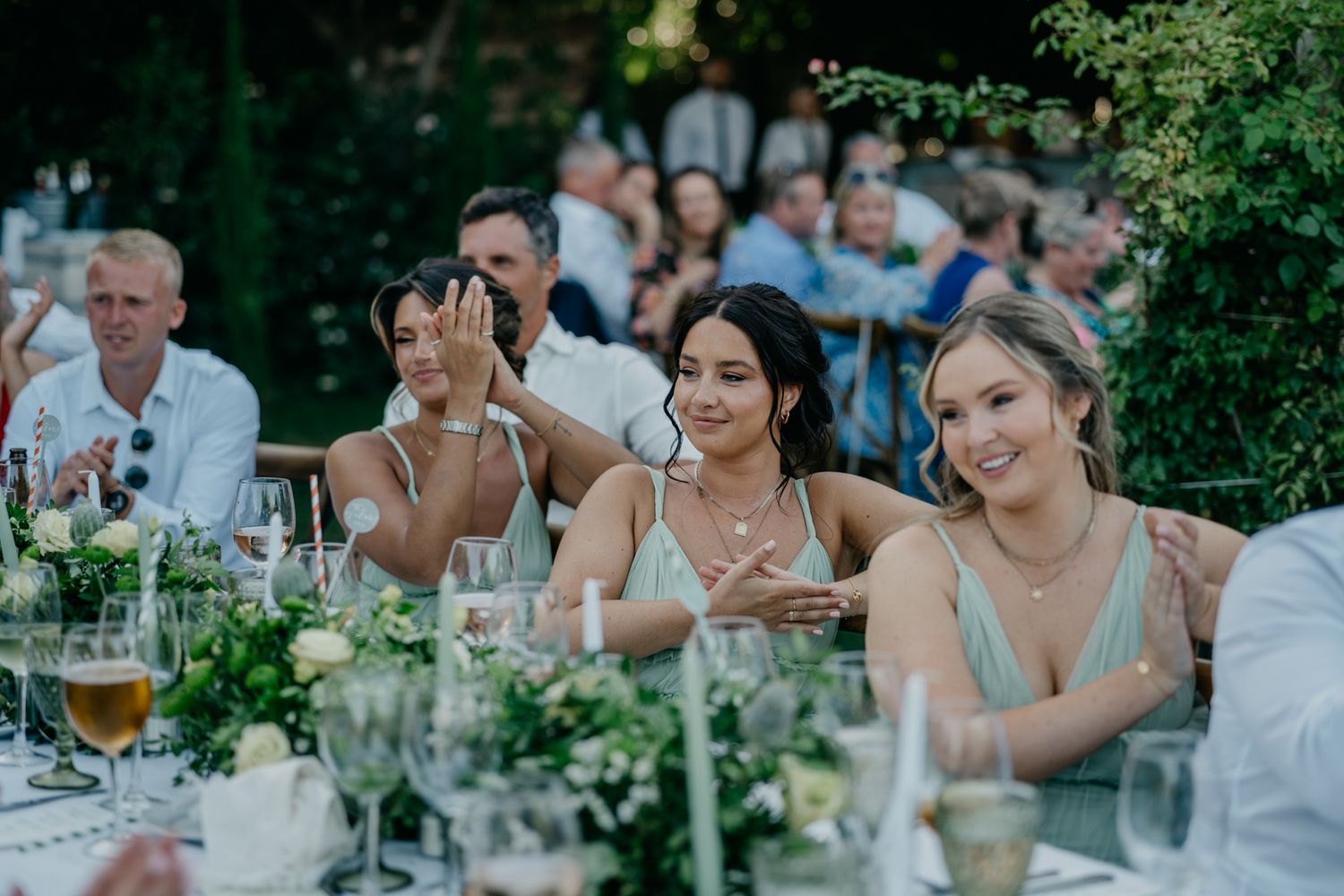 Wedding guests gathered at outdoor reception tables with floral centerpieces.