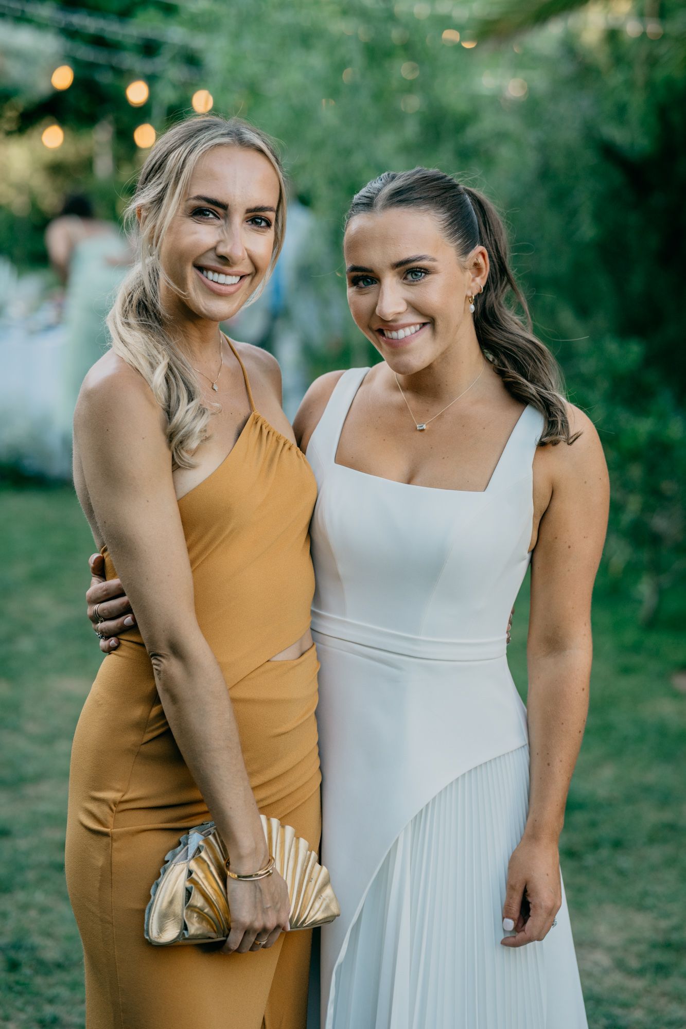 Two wedding guests pose together in formal dresses at outdoor celebration.