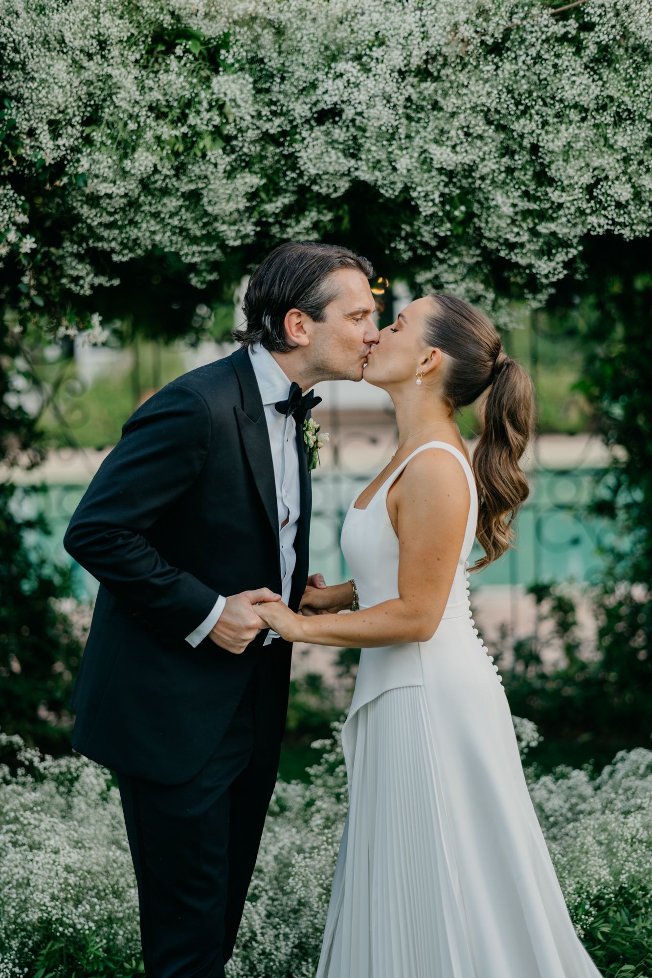 Wedding couple sharing a romantic kiss under blooming white flowers.