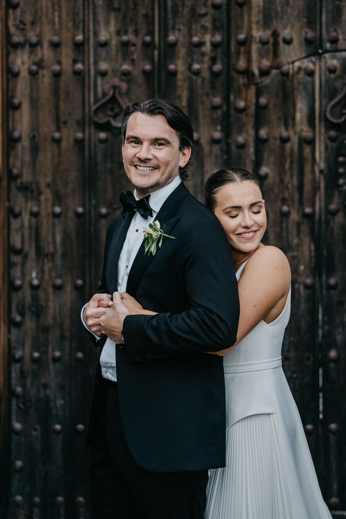 Elegant couple shares intimate moment in front of vintage wooden door at their wedding.