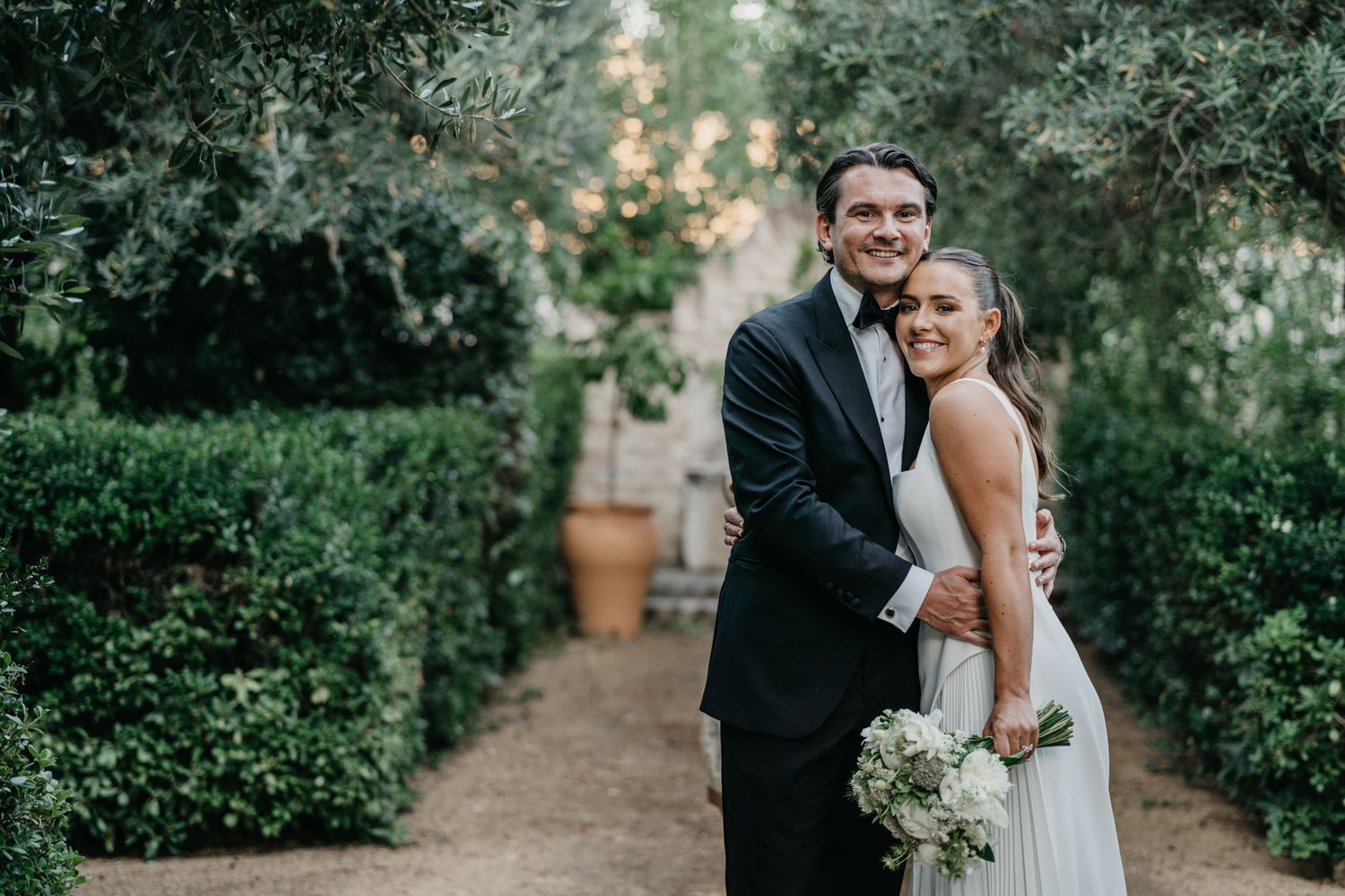Bride and groom embrace in lush garden setting with soft natural lighting.