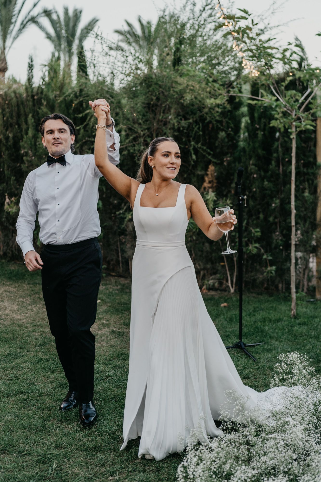Couple celebrates during wedding reception in garden setting with palm trees.