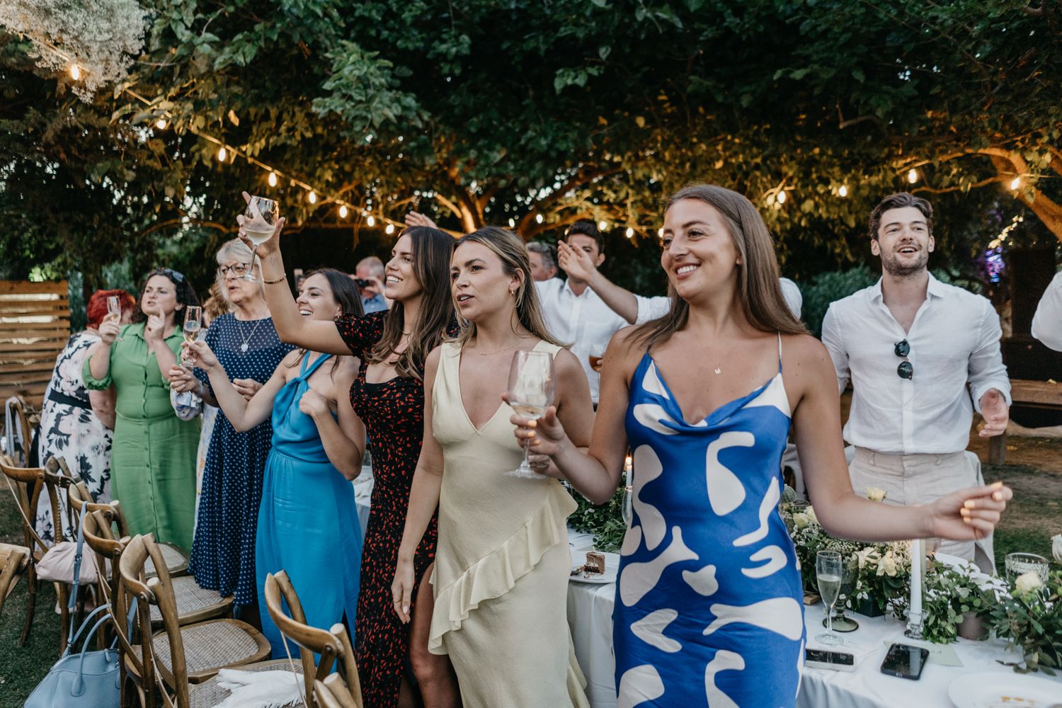 Wedding guests dance and celebrate under string lights at outdoor reception.