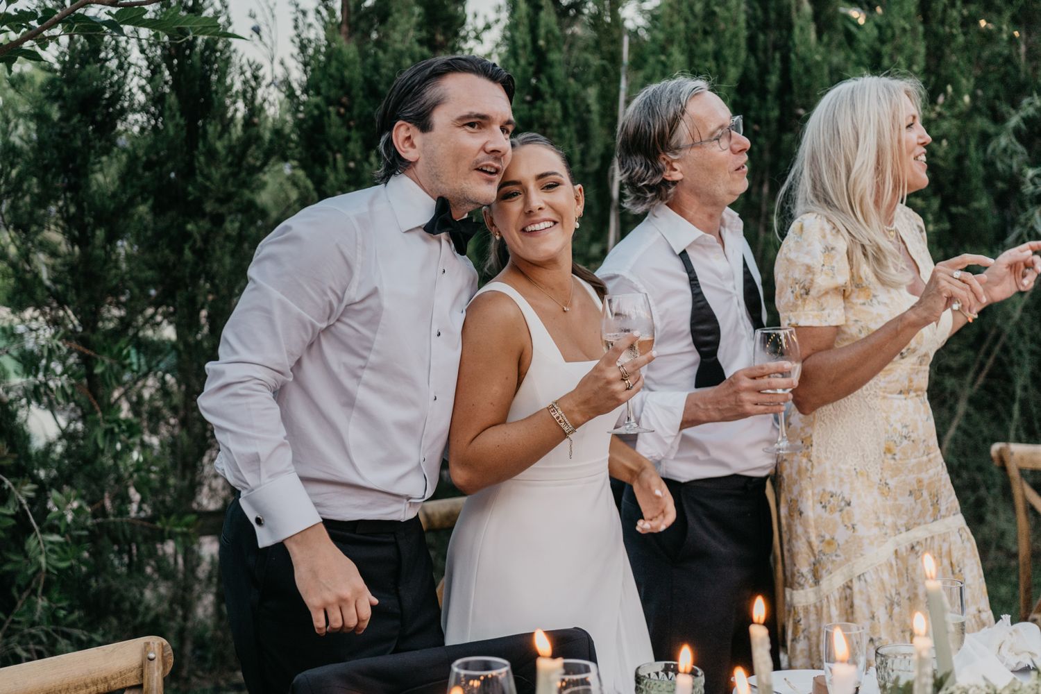 Wedding guests raise glasses for a celebratory toast during an outdoor garden reception celebration.