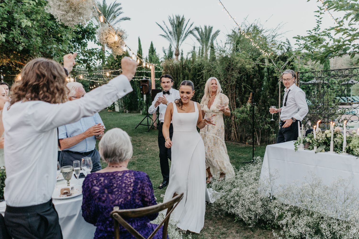 Guests celebrate at an outdoor wedding reception with champagne toasts in a lush garden setting.