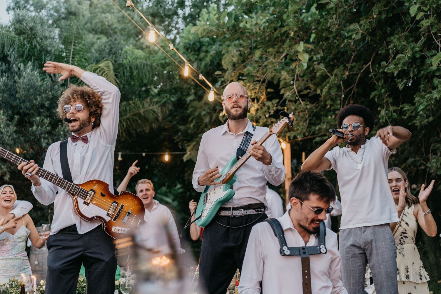 Band performs energetically on stage with guitars at outdoor wedding reception.