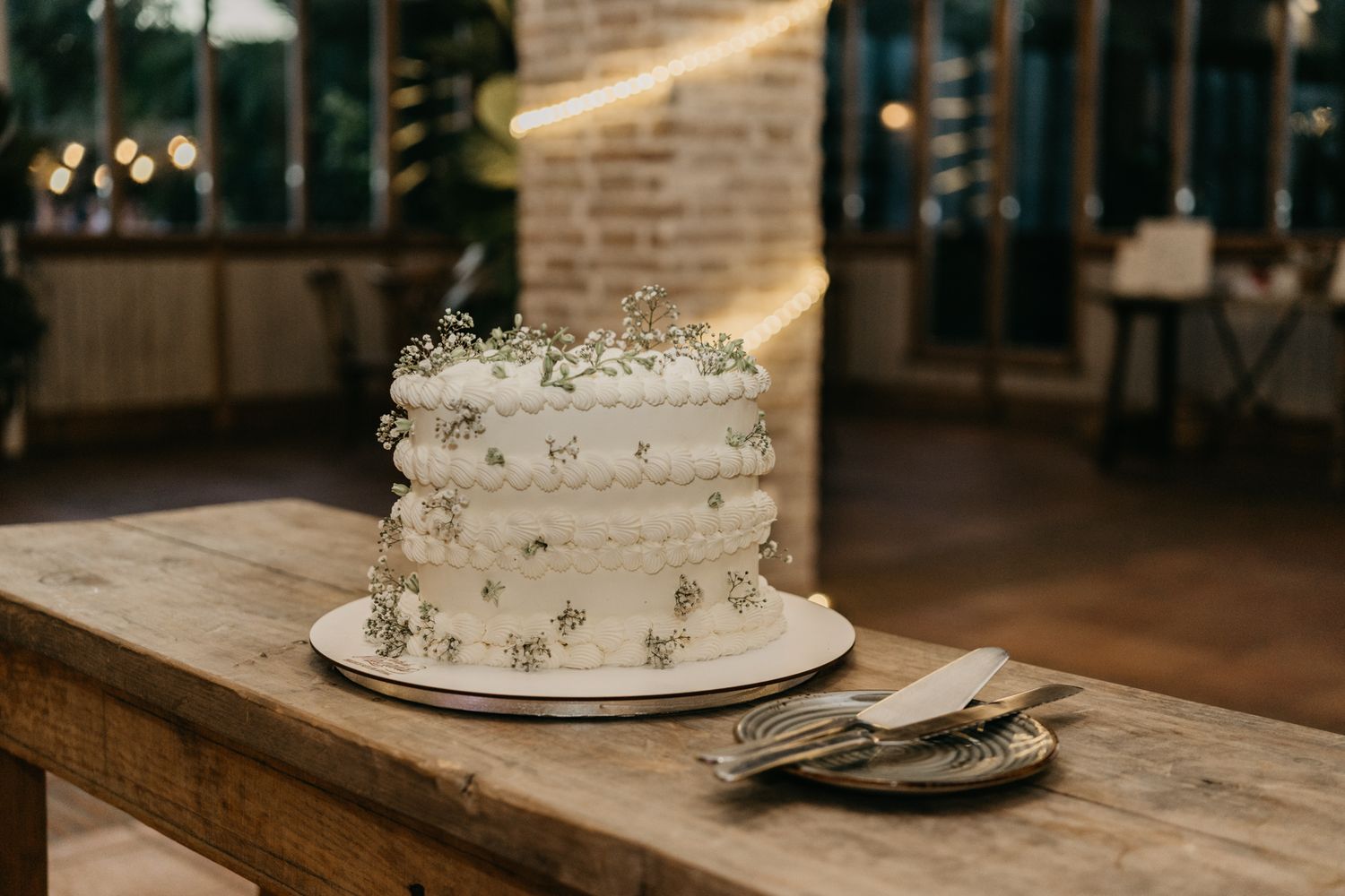 Elegant white wedding cake with delicate floral details displayed on wooden table.