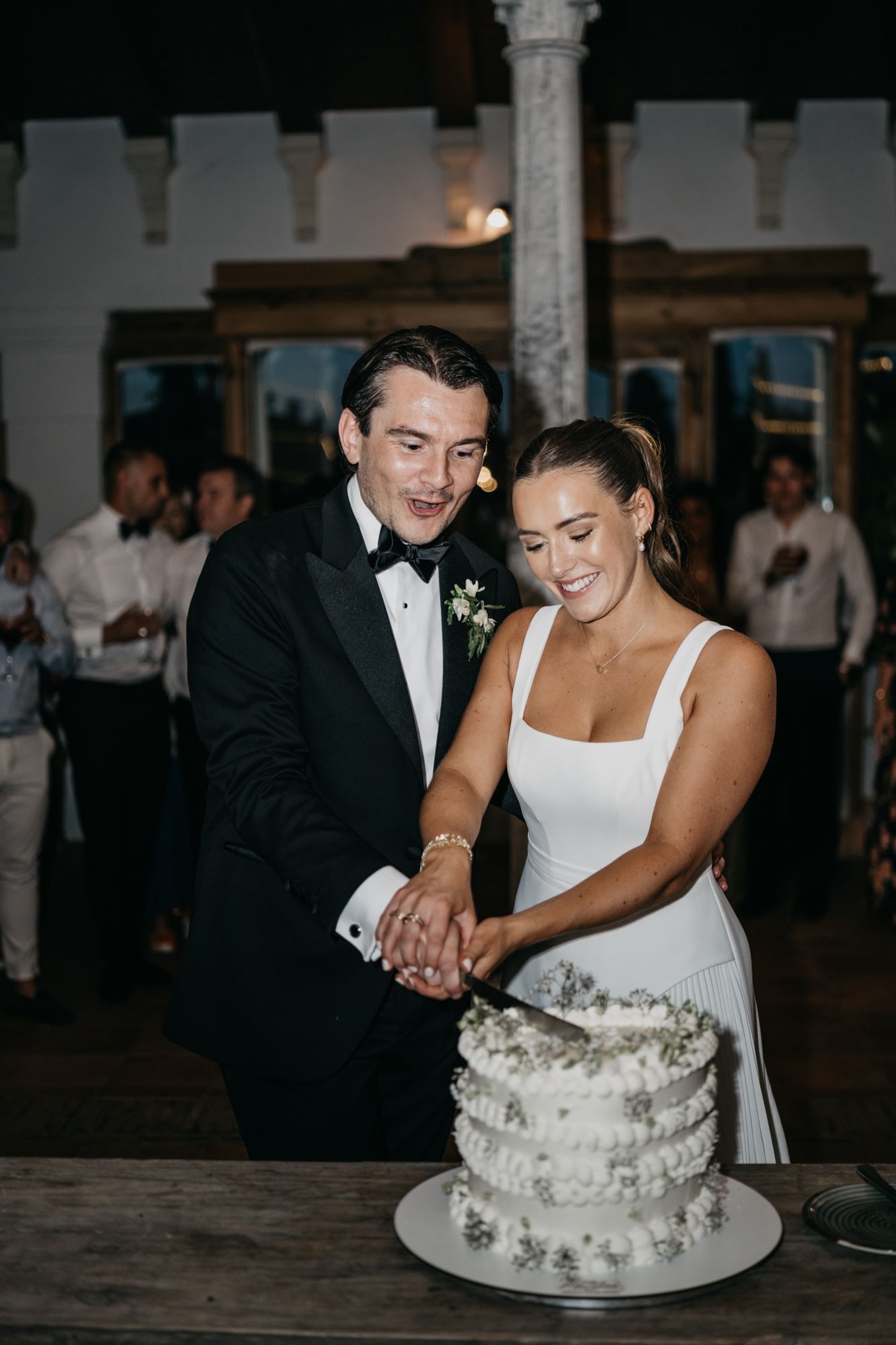 Newlyweds cut their elegant white wedding cake together during their reception.