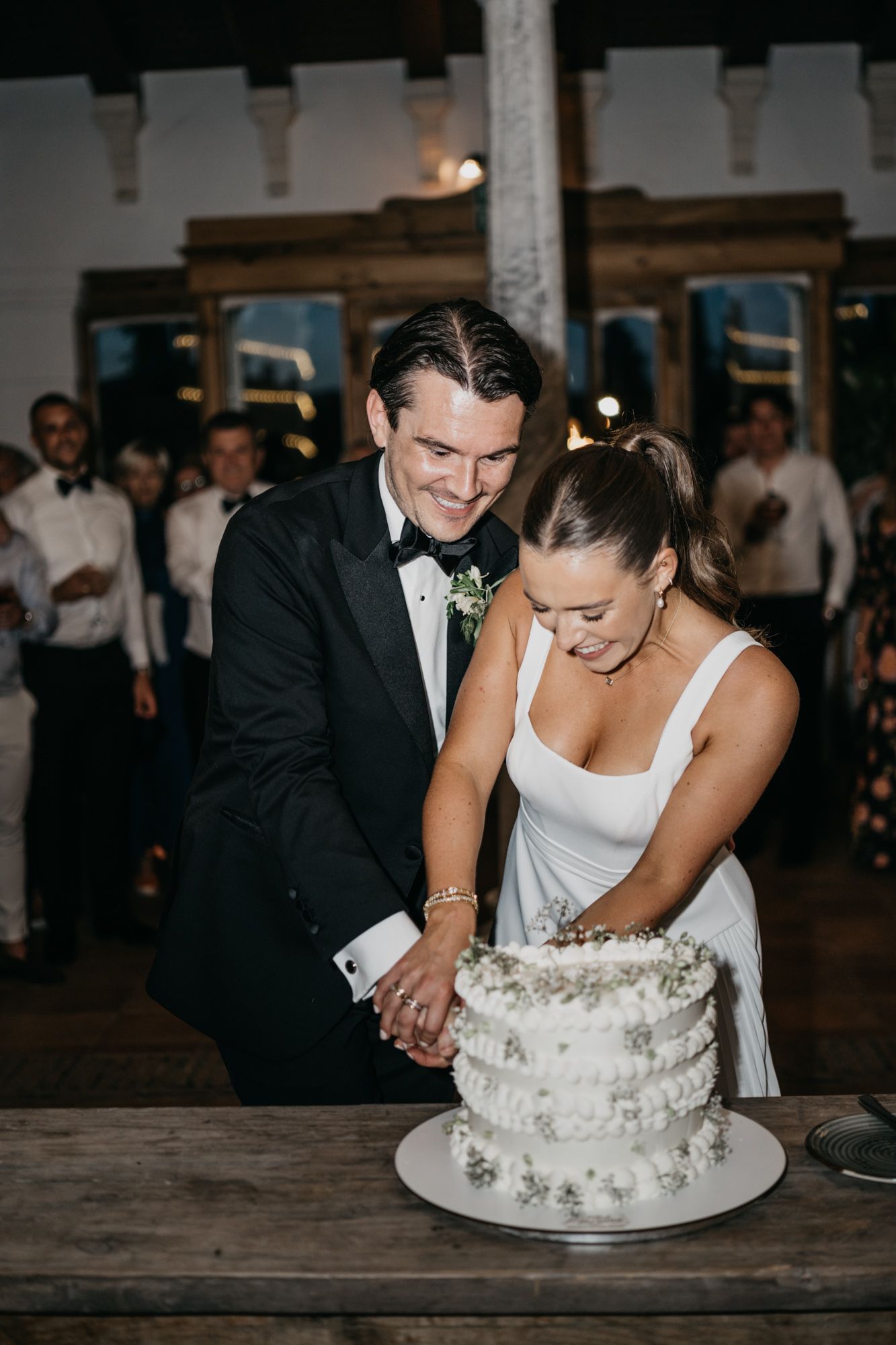Couple shares a sweet moment while cutting their white floral wedding cake.