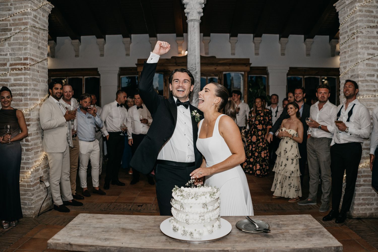 Happy couple shares a joyful moment while cutting their wedding cake at their reception.