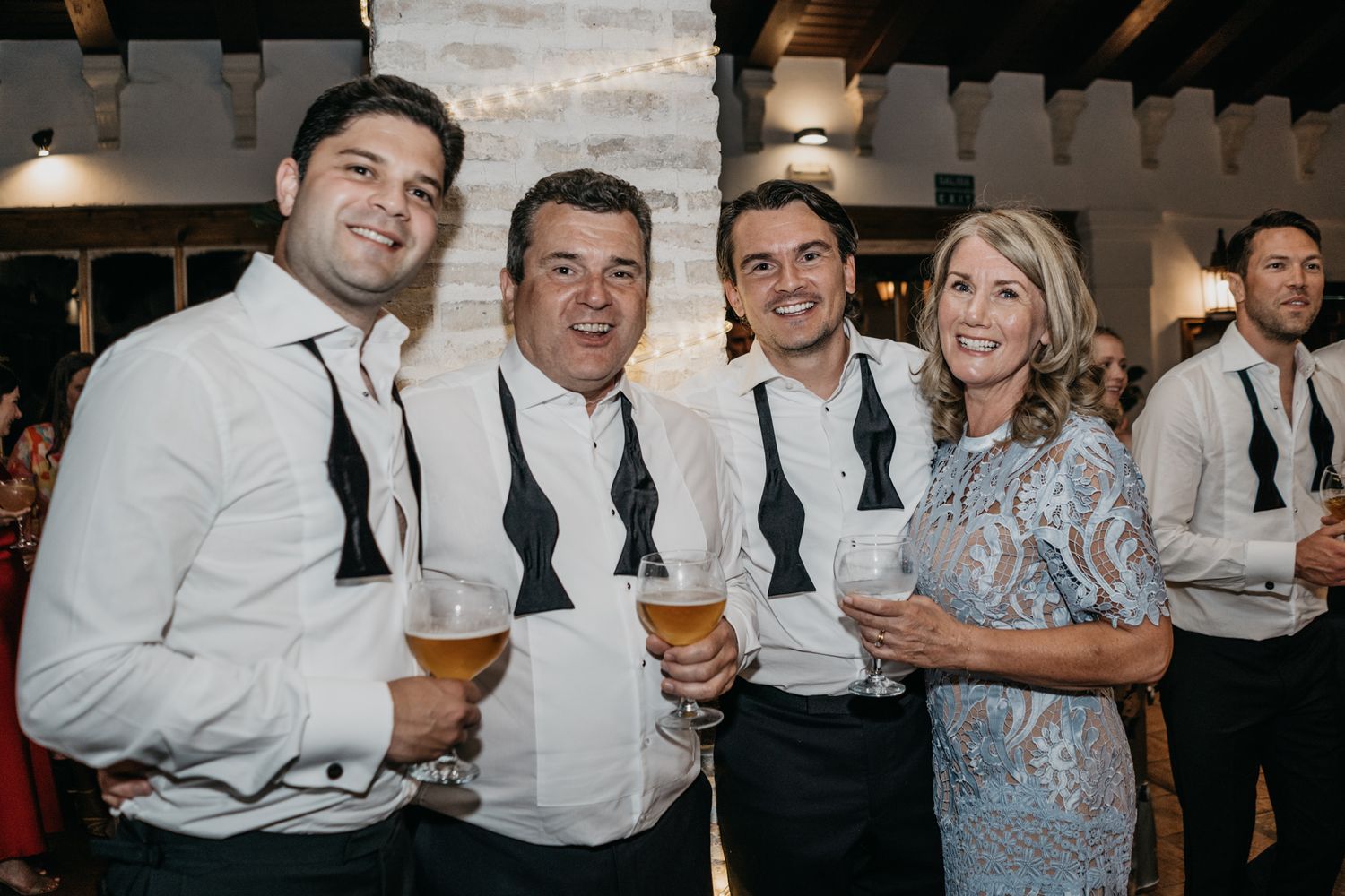 Wedding reception guests in formal attire pose together with drinks.