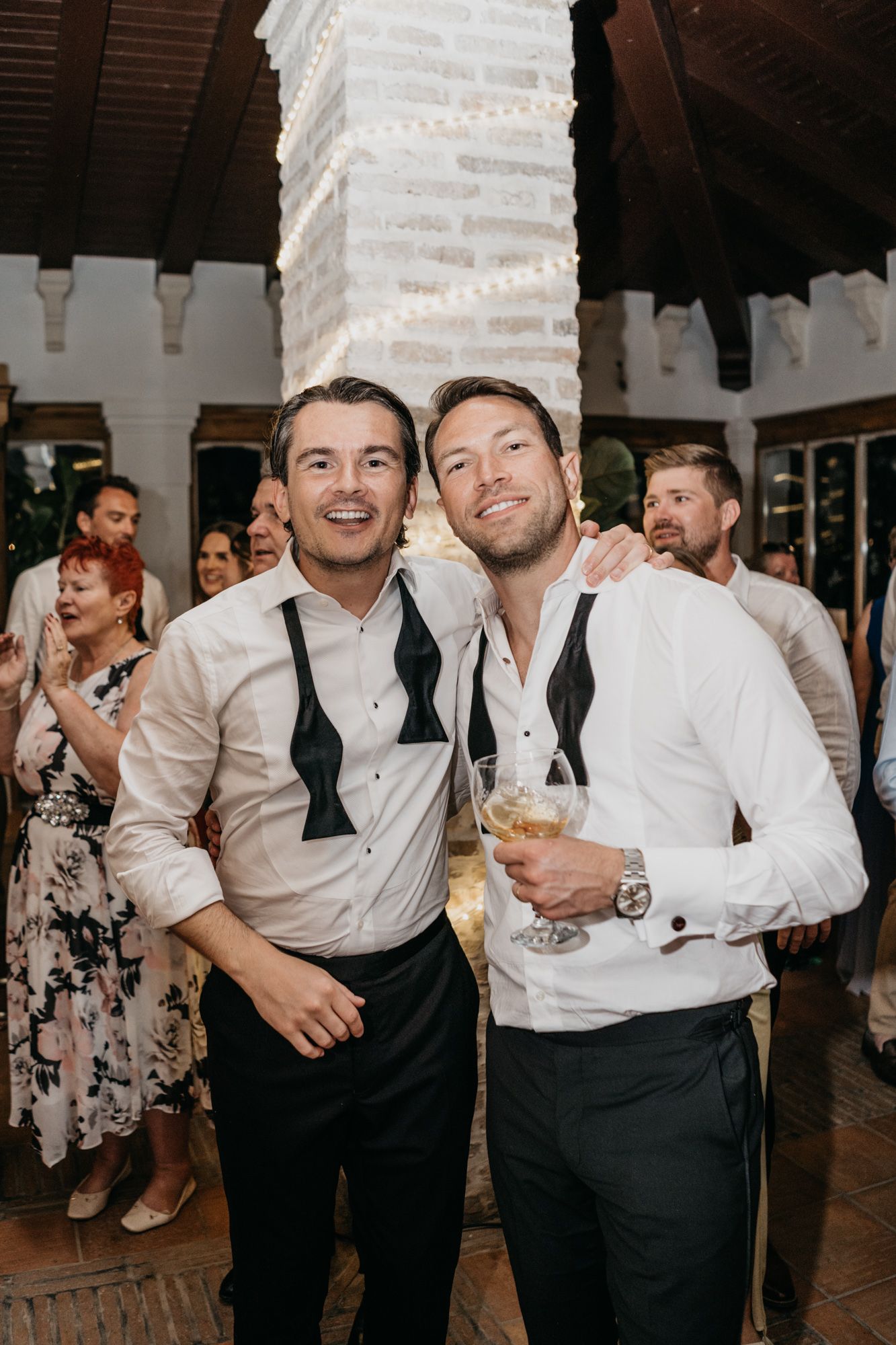Wedding guests in suspenders and formal attire celebrating at an indoor reception venue.