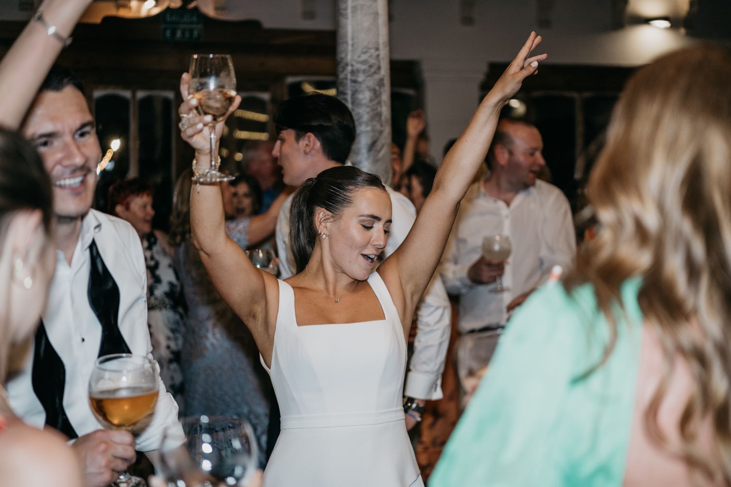 A bride celebrates with raised arms during her wedding reception party.