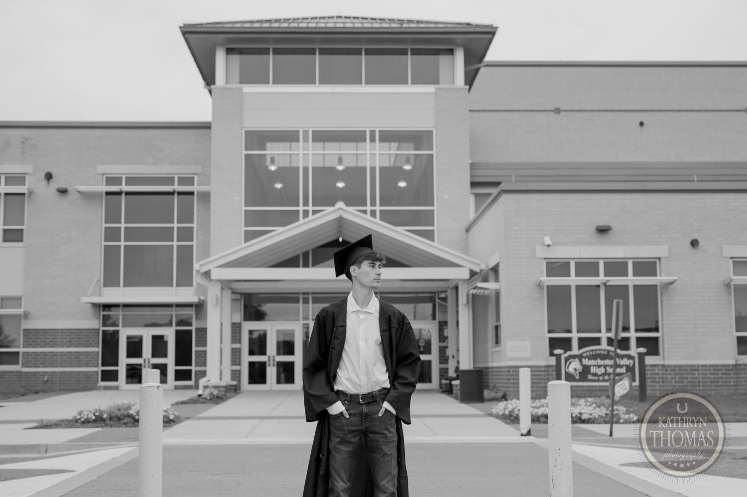 Black and white portrait of graduate in front of modern school building.