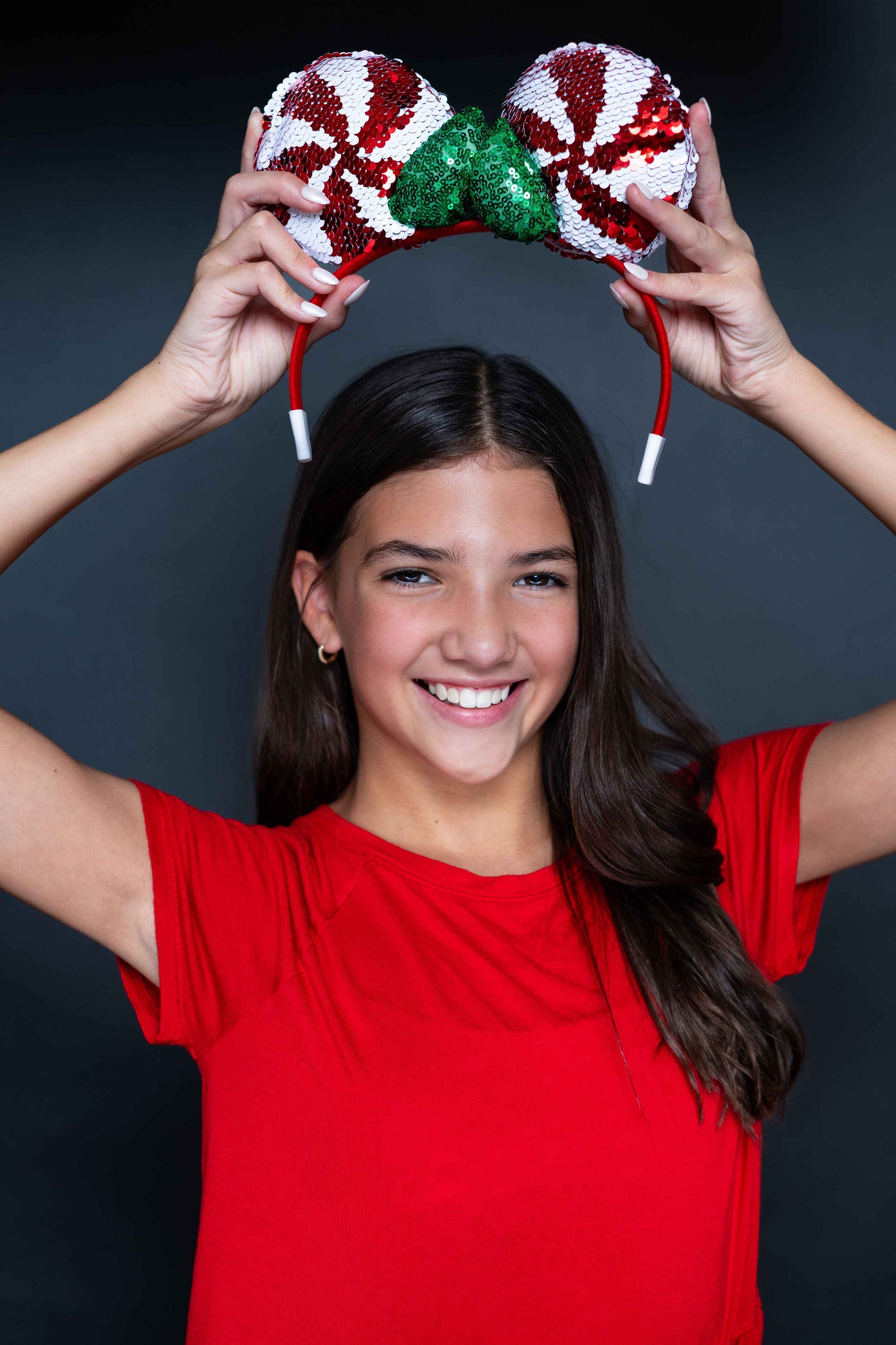 Person in red shirt holding sparkly peppermint candy themed mouse ears overhead modeling for Hug A Band.