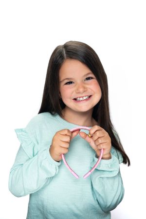 Child in mint sweater holding pink headband against white background modeling for Hug A Band.