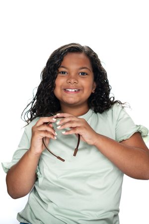 Child wearing mint green shirt holding sunglasses with curly hair against white background modeling for Hug A Band.
