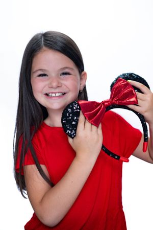 Child in red shirt holding black and red bow Mickey ears against white backgroundmodeling for Hug A Band.