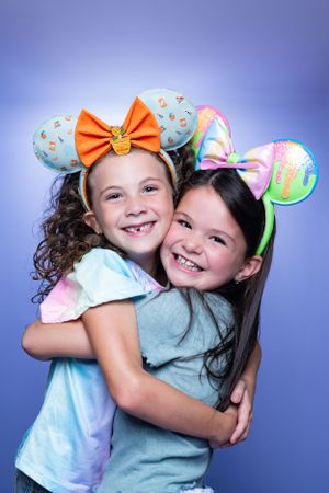 Two children wearing Disney-themed ear headbands hugging and smiling against purple background modeling for Hug A Band.