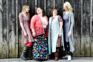Four women in vintage-style dresses pose against rustic wooden wall modeling Lula Roe