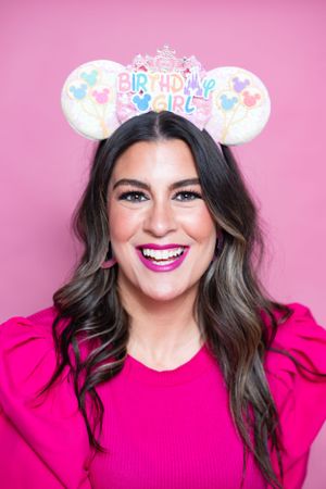 Birthday-themed sparkly mouse ears with pastel decorations on pink background modeling for The Minnie Castle.