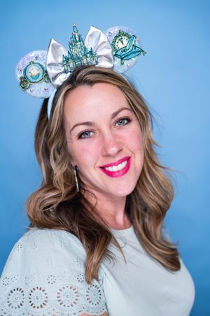 Elegant Disney-inspired castle and carriage Mickey ears headband with white bow against blue backdrop modeling for The Minnie Castle.