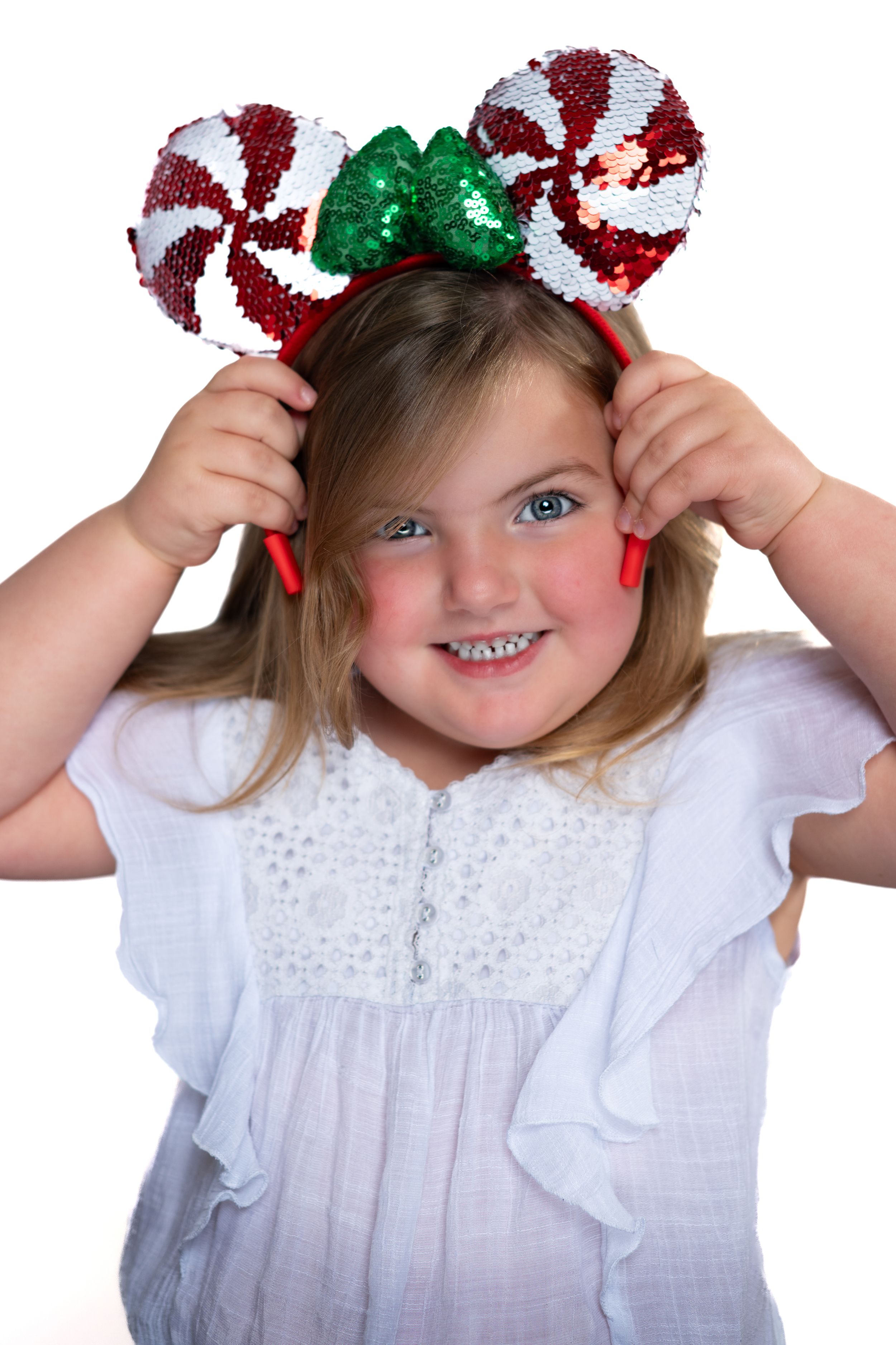 The child is wearing festive peppermint candy cane Mickey Mouse ears with green bow modeling for Hug A Band.