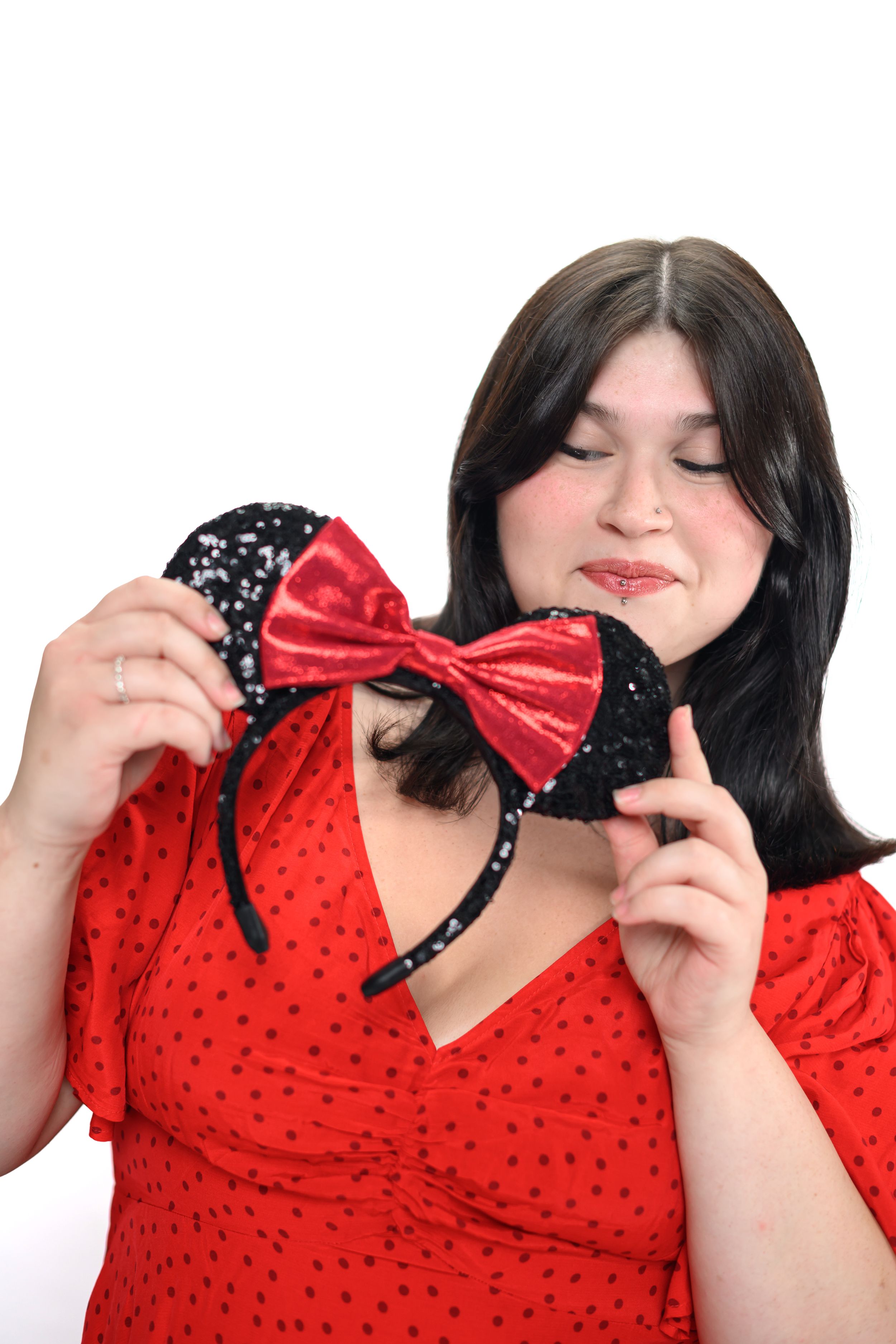 Woman in red polka dot dress holding black and red Minnie Mouse ears modeling for Hug A Band.