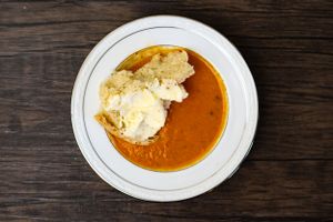 Bowl of creamy orange soup with floating bread on white plate. Local Chef