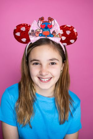Stitch-themed Mickey ears with hearts and red bow against pink backdrop modeling for The Minnie Castle.