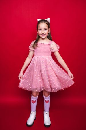 Child in pink polka dot dress and cat ears posing against red backdrop wearing Sparkle In Pink.