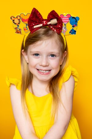 Winnie the Pooh themed Mickey ears with red sequin bow on yellow background modeling for The Minnie Castle.