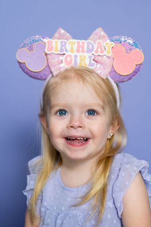 Purple and pink Birthday Girl mouse ears headband on blue background modeling for The Minnie Castle.