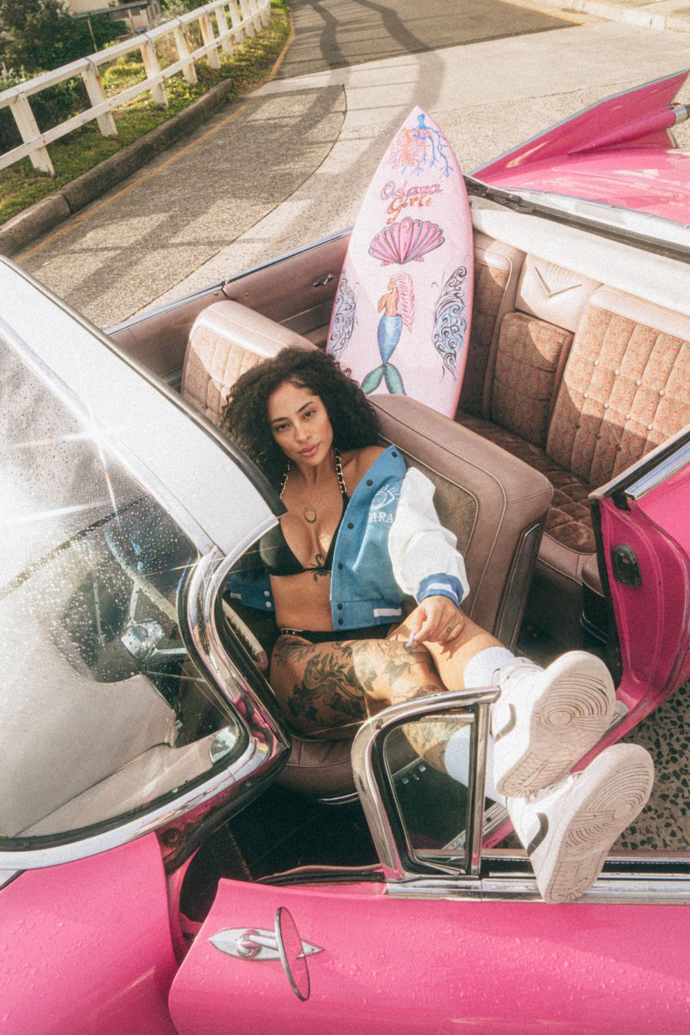 Model posing in a vintage pink convertible wearing casual street style and swimwear.