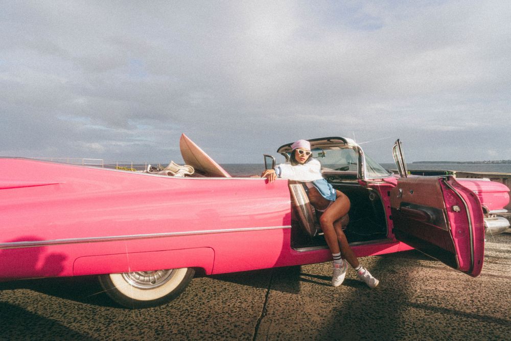 Pink classic Cadillac convertible parked on scenic coastal road.