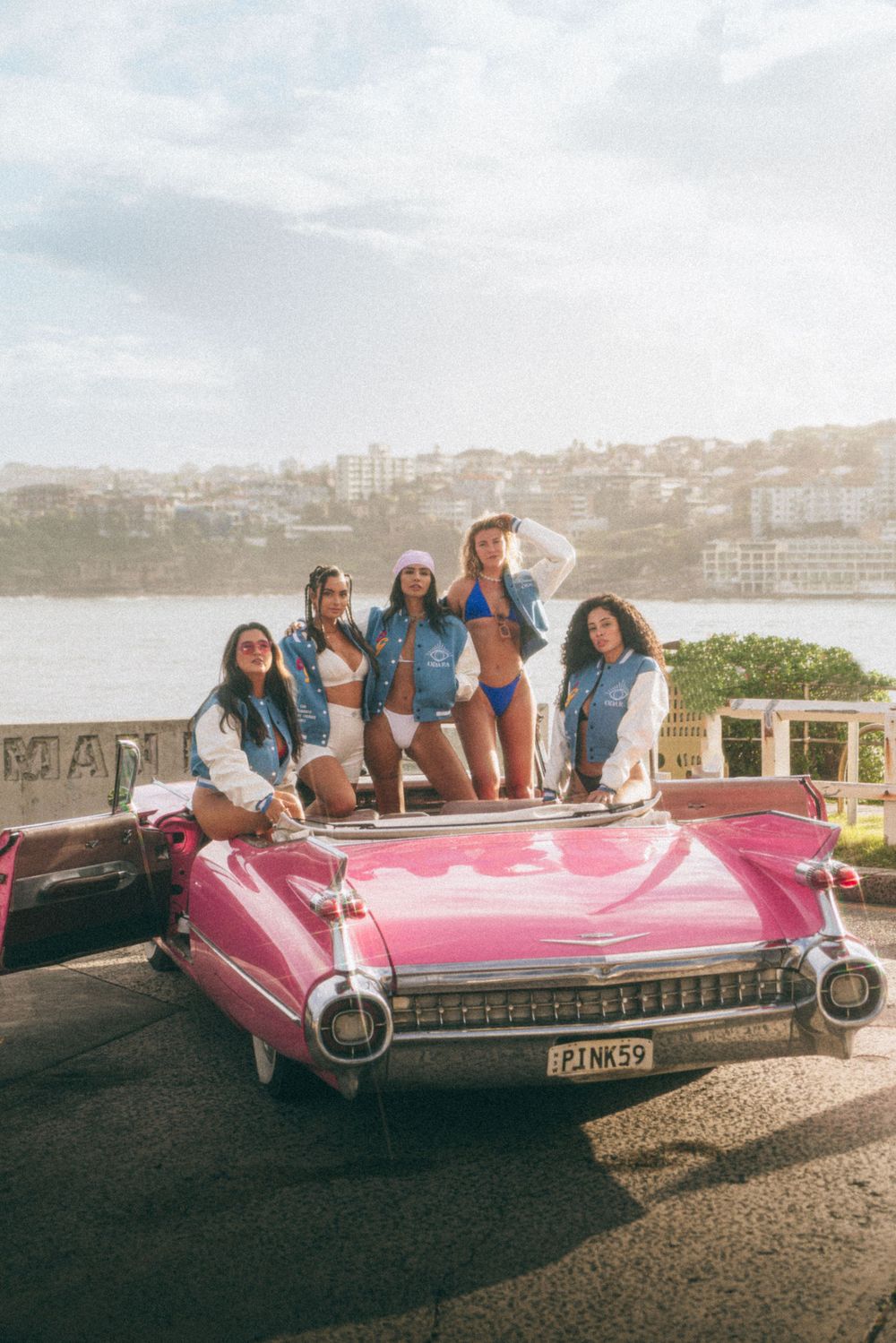 Group enjoying summer day posing on pink vintage Cadillac with ocean view.