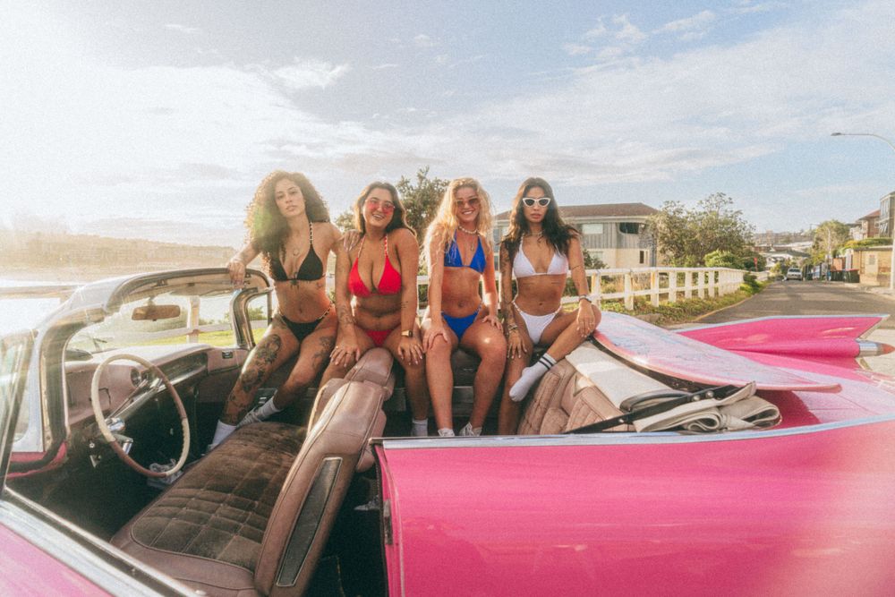 Group lounging in vintage pink Cadillac during beachside photoshoot.