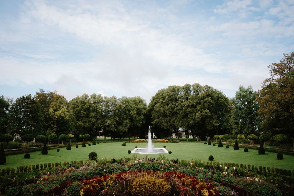 Wide landscape view of manicured gardens with fountains under a cloudy sky.
