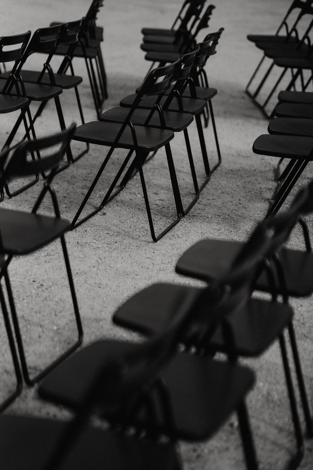 Empty black folding chairs arranged in rows for an outdoor ceremony.