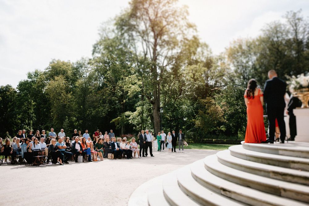 Panoramic view of wedding guests seated on white chairs along curved stone steps.