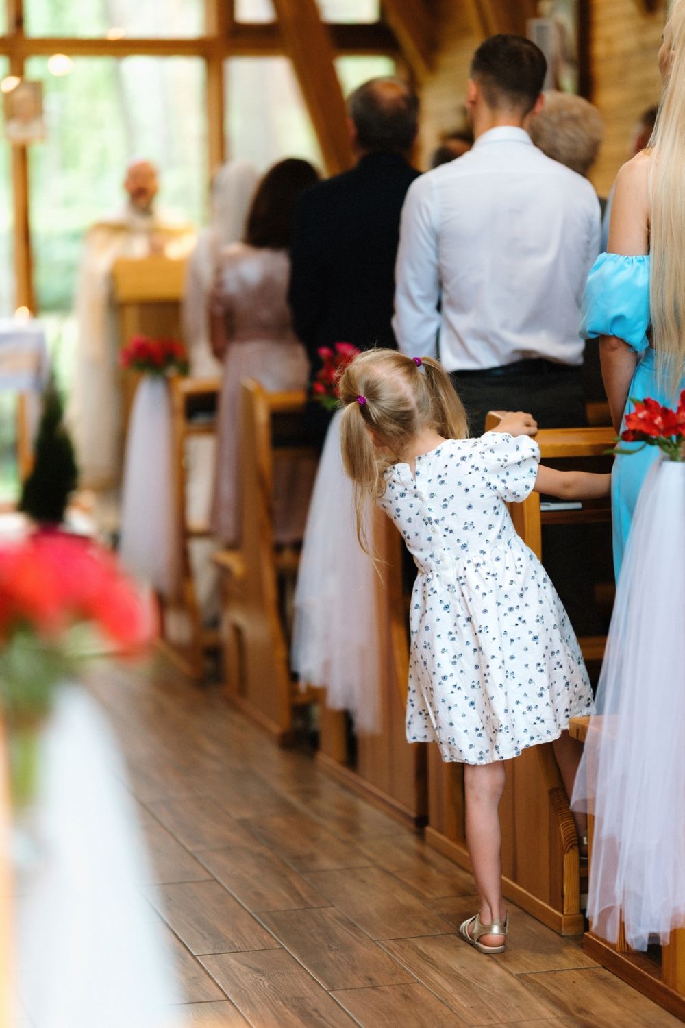 A young girl in a polka dot dress walks down a church aisle during a wedding ceremony.