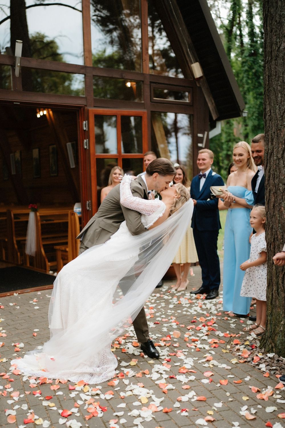 Newlyweds share romantic dip kiss surrounded by flying flower petals.