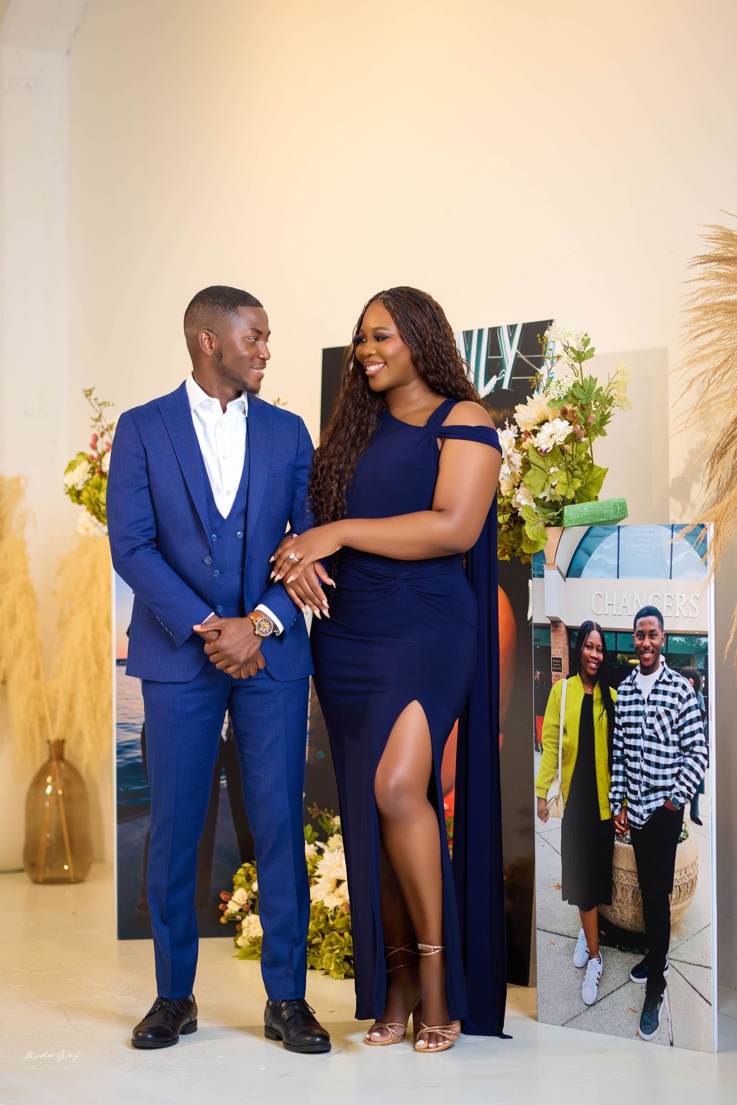 Couple in formal blue attire share intimate moment during photo session with decorative backdrop.